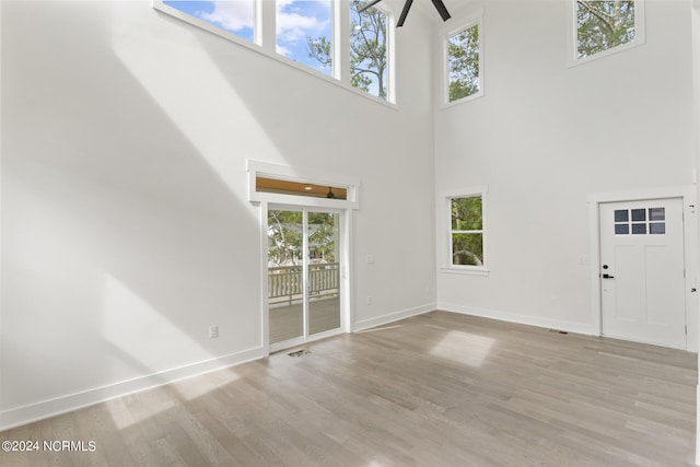 unfurnished living room with light hardwood / wood-style floors, ceiling fan, a high ceiling, and a wealth of natural light