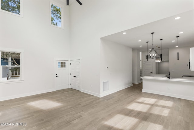 unfurnished living room featuring ceiling fan with notable chandelier, sink, light hardwood / wood-style flooring, and a high ceiling