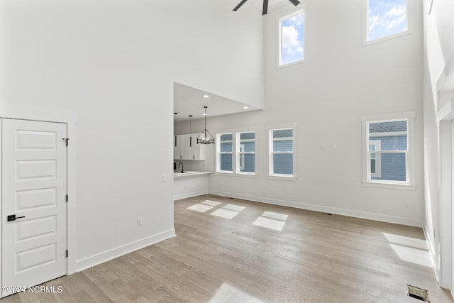 unfurnished living room featuring sink, light hardwood / wood-style floors, ceiling fan with notable chandelier, and a towering ceiling