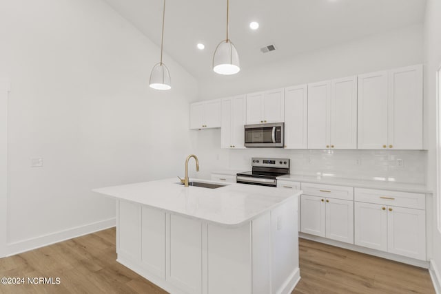 kitchen with appliances with stainless steel finishes, a kitchen island with sink, light hardwood / wood-style flooring, sink, and decorative light fixtures