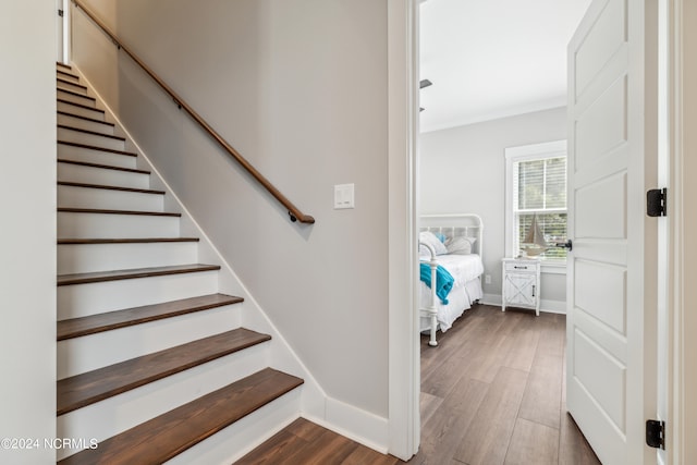 stairs with wood-type flooring and ornamental molding