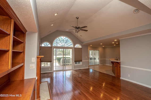 unfurnished living room featuring sink, a textured ceiling, dark hardwood / wood-style floors, ceiling fan, and high vaulted ceiling