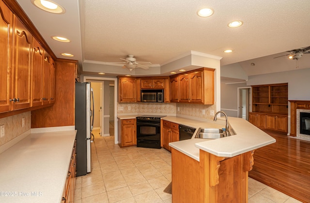 kitchen featuring kitchen peninsula, black appliances, sink, ceiling fan, and a kitchen bar