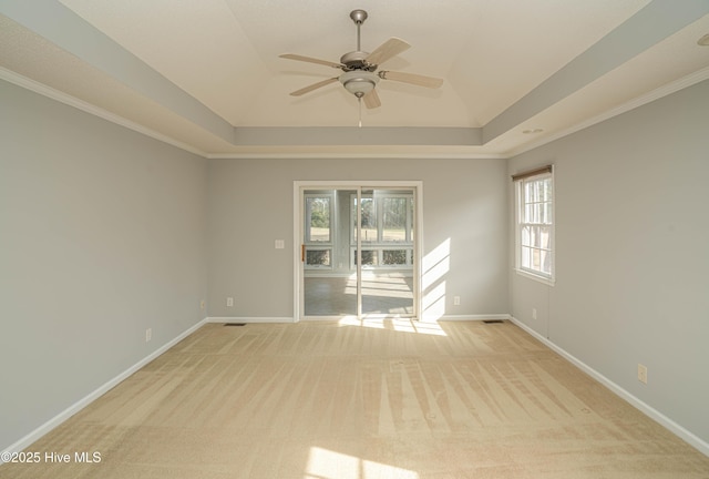 empty room featuring ceiling fan, a tray ceiling, light colored carpet, and crown molding