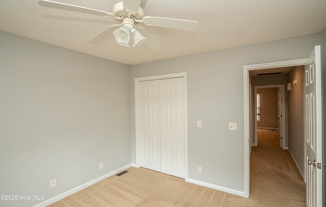 unfurnished bedroom with a textured ceiling, a closet, ceiling fan, and light colored carpet