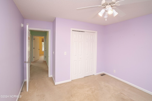 unfurnished bedroom with a textured ceiling, ceiling fan, a closet, and light carpet