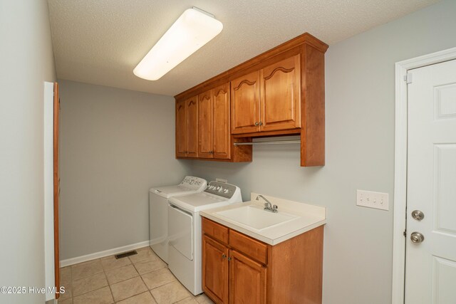 washroom featuring sink, washing machine and clothes dryer, light tile patterned flooring, a textured ceiling, and cabinets