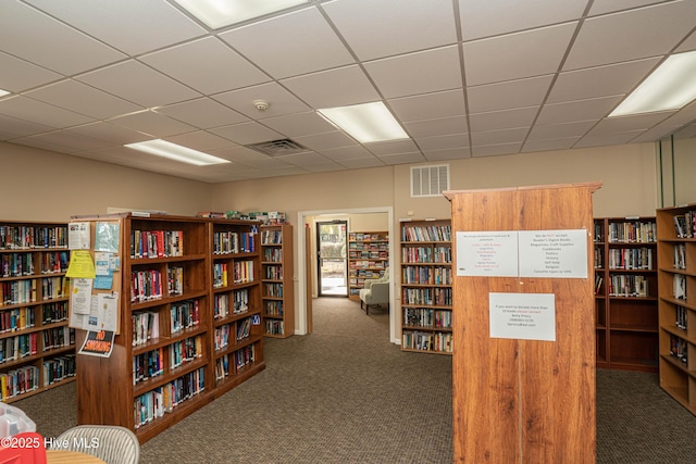 living area with a drop ceiling and dark colored carpet