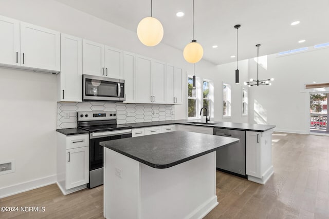 kitchen with dark countertops, a sink, light wood finished floors, a peninsula, and stainless steel appliances