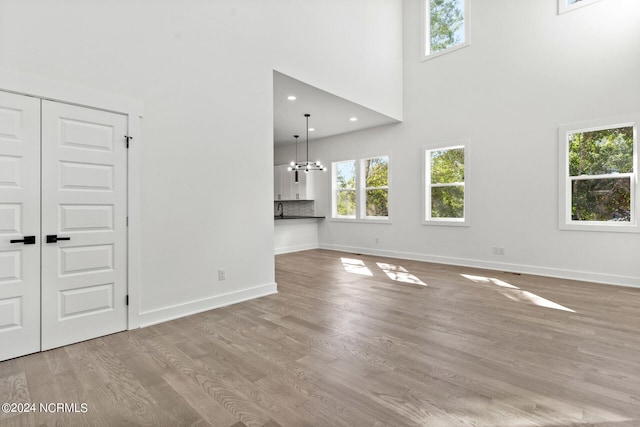 unfurnished living room with light hardwood / wood-style floors, an inviting chandelier, and a towering ceiling