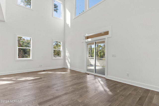 unfurnished living room featuring a towering ceiling, a healthy amount of sunlight, and dark hardwood / wood-style flooring