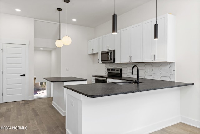 kitchen with dark countertops, appliances with stainless steel finishes, a sink, wood finished floors, and backsplash