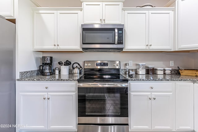 kitchen featuring white cabinetry, stainless steel appliances, and dark stone counters