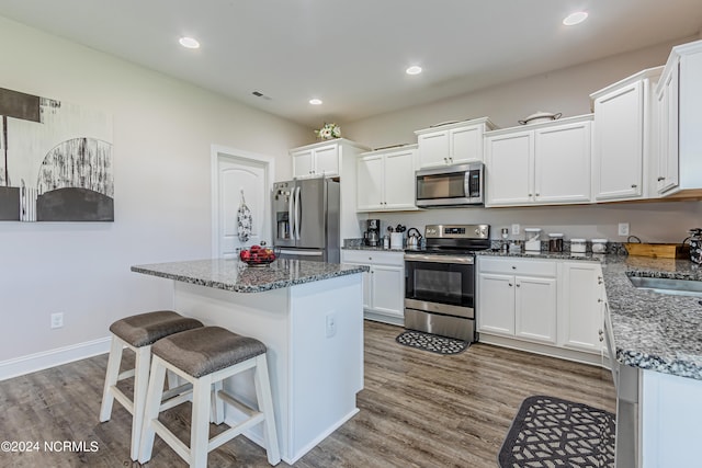 kitchen featuring white cabinets, a center island, appliances with stainless steel finishes, and dark stone counters