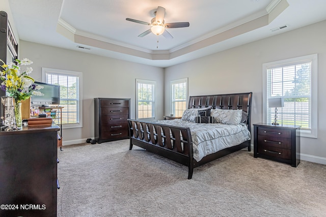 bedroom with ceiling fan, light colored carpet, a tray ceiling, and multiple windows