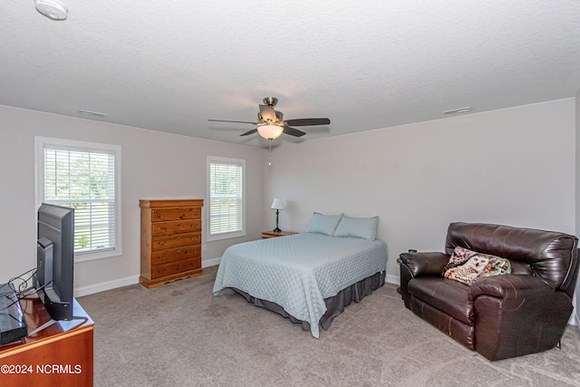 bedroom with ceiling fan, light colored carpet, and a textured ceiling