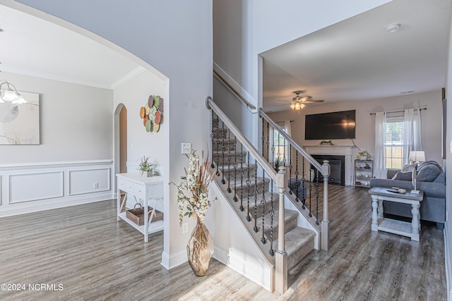 staircase with ceiling fan, a fireplace, wood-type flooring, and crown molding