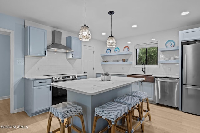 kitchen with tasteful backsplash, wall chimney exhaust hood, stainless steel appliances, light wood-type flooring, and a center island