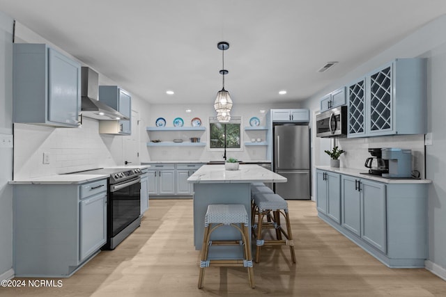 kitchen with light stone counters, light hardwood / wood-style floors, a kitchen island, wall chimney exhaust hood, and stainless steel appliances