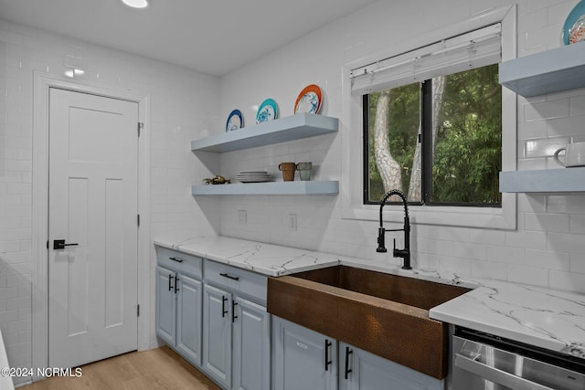 kitchen featuring light stone counters, sink, stainless steel dishwasher, light hardwood / wood-style flooring, and decorative backsplash