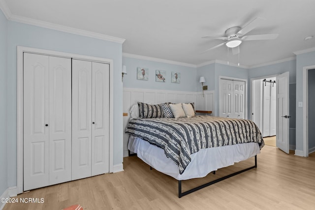 bedroom with ornamental molding, light wood-type flooring, two closets, and ceiling fan