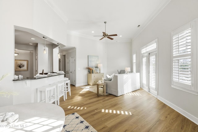 living room featuring crown molding, light hardwood / wood-style flooring, ceiling fan, and a high ceiling