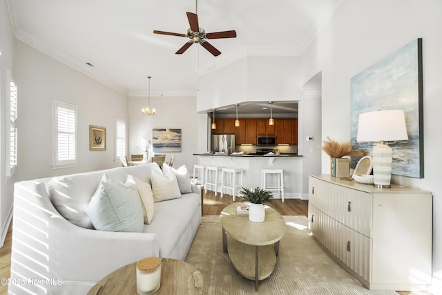 living room with ornamental molding, ceiling fan with notable chandelier, and light hardwood / wood-style flooring