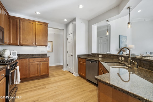 kitchen featuring appliances with stainless steel finishes, decorative light fixtures, sink, dark stone counters, and light wood-type flooring