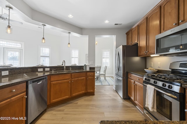 kitchen featuring decorative light fixtures, sink, dark stone counters, stainless steel appliances, and light hardwood / wood-style flooring