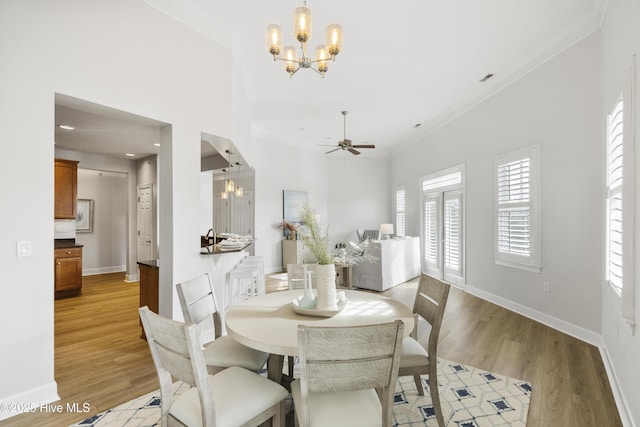 dining room with crown molding, light hardwood / wood-style flooring, ceiling fan with notable chandelier, and a towering ceiling