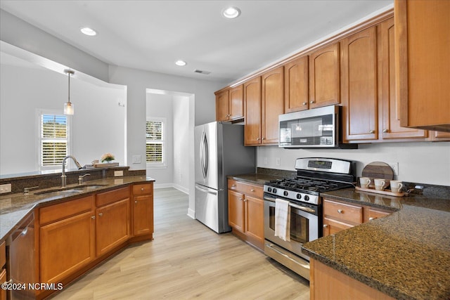 kitchen featuring sink, dark stone countertops, light wood-type flooring, appliances with stainless steel finishes, and pendant lighting