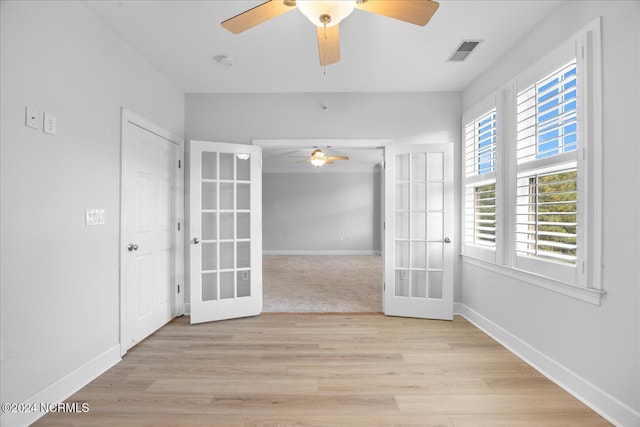 empty room with ceiling fan, light hardwood / wood-style floors, and french doors