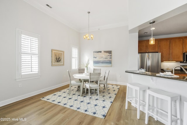 dining space with crown molding, sink, an inviting chandelier, and light wood-type flooring