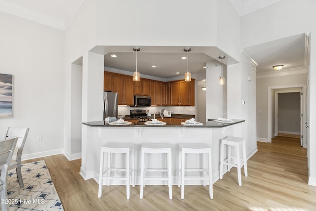 kitchen with stainless steel appliances, ornamental molding, decorative light fixtures, kitchen peninsula, and dark stone counters