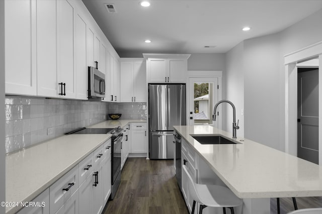 kitchen featuring a breakfast bar area, sink, a center island with sink, appliances with stainless steel finishes, and dark hardwood / wood-style flooring