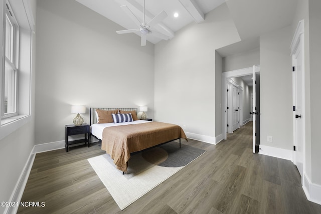 bedroom featuring ceiling fan, beamed ceiling, hardwood / wood-style floors, and a high ceiling