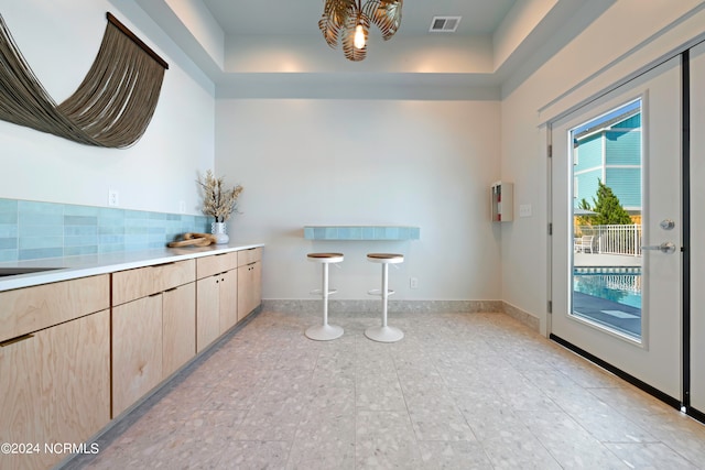 kitchen featuring decorative backsplash, light brown cabinets, and a raised ceiling