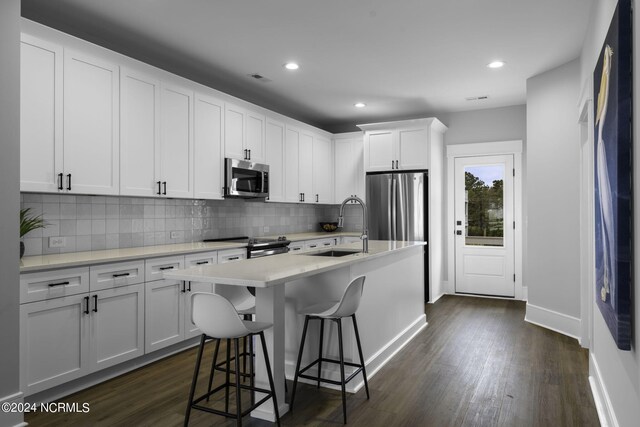 kitchen with appliances with stainless steel finishes, white cabinets, a breakfast bar area, dark hardwood / wood-style flooring, and a center island with sink