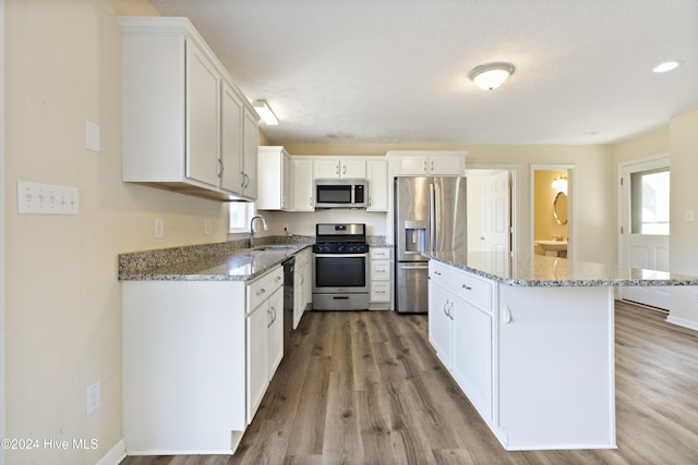 kitchen featuring light stone counters, stainless steel appliances, white cabinets, a center island, and light hardwood / wood-style floors