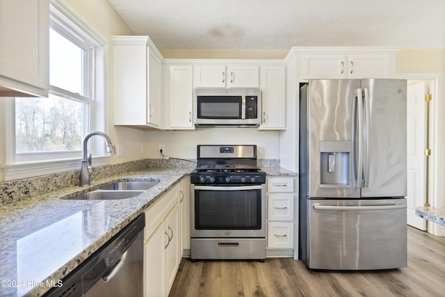 kitchen with white cabinets, sink, appliances with stainless steel finishes, light hardwood / wood-style floors, and light stone counters