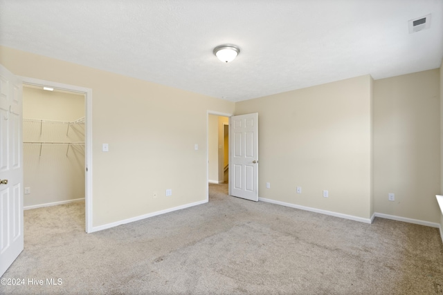 unfurnished bedroom with light colored carpet, a walk in closet, and a closet