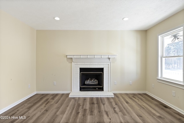 unfurnished living room featuring wood-type flooring, a textured ceiling, and a brick fireplace