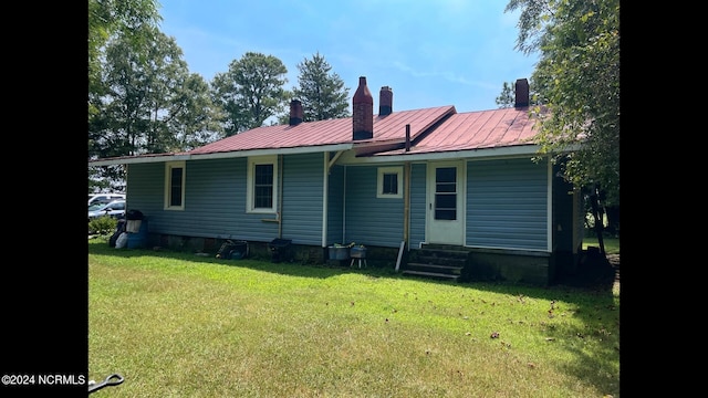 back of house with entry steps, a chimney, metal roof, and a yard