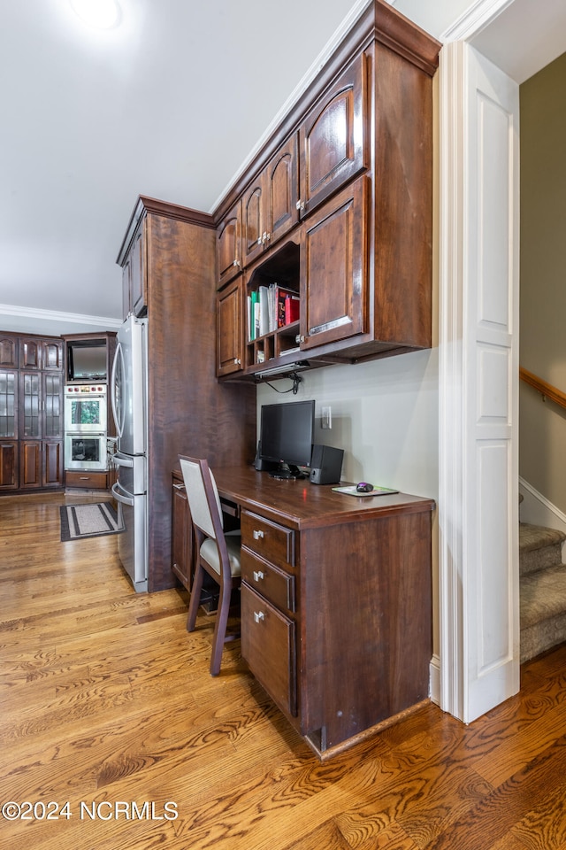 office area featuring ornamental molding, built in desk, and light hardwood / wood-style floors