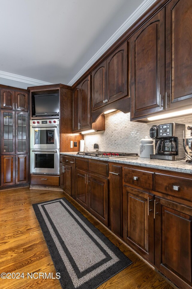 kitchen with crown molding, appliances with stainless steel finishes, dark hardwood / wood-style flooring, and tasteful backsplash