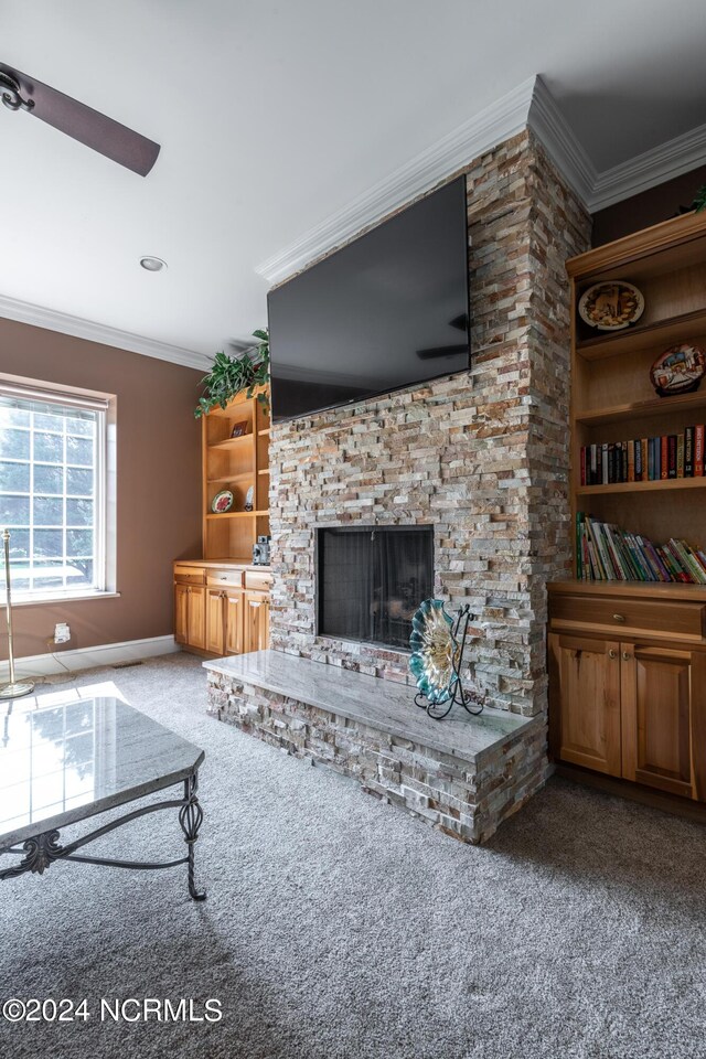 living room with crown molding, built in shelves, carpet, a stone fireplace, and ceiling fan