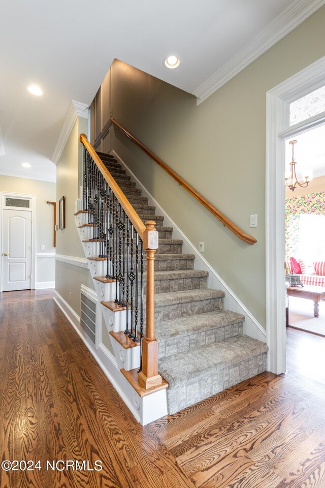 stairway featuring hardwood / wood-style floors, ornamental molding, an inviting chandelier, and a healthy amount of sunlight