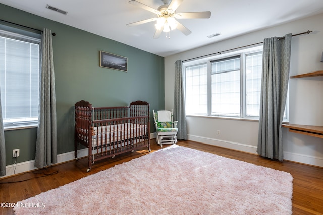 bedroom with a nursery area, hardwood / wood-style flooring, and ceiling fan