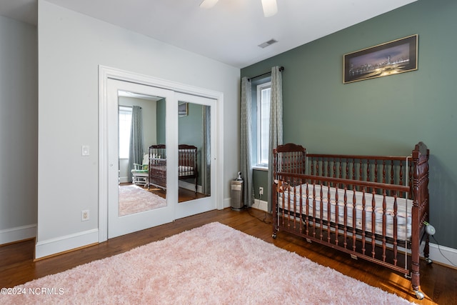 bedroom featuring dark hardwood / wood-style flooring, a nursery area, and ceiling fan