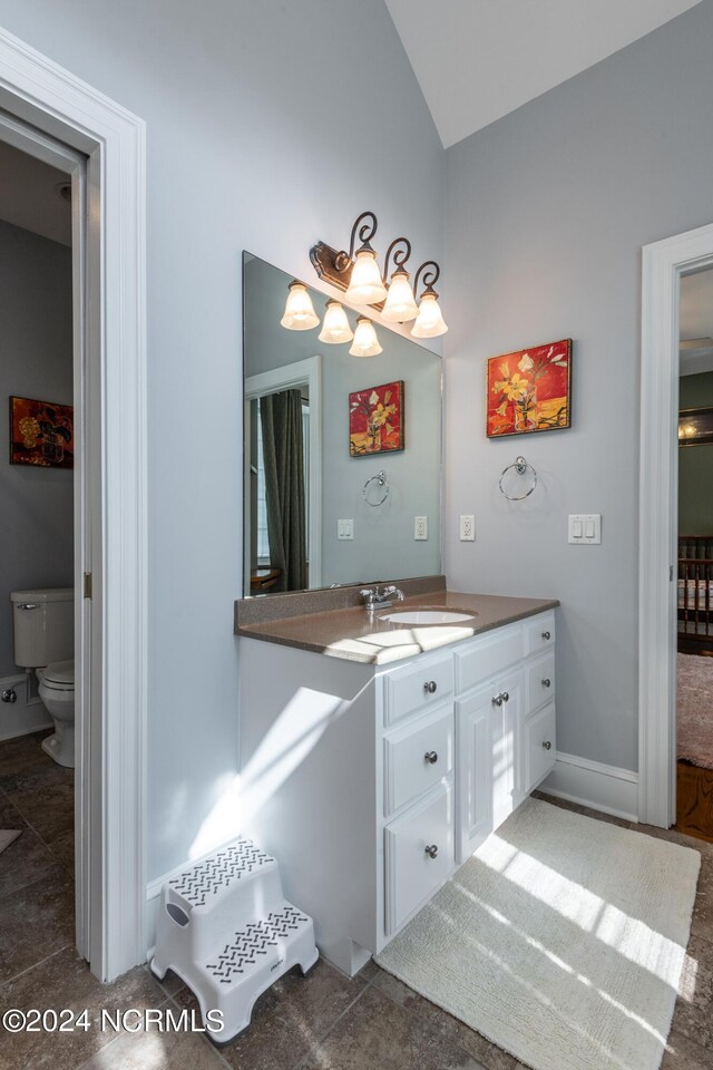 bathroom with vanity, toilet, vaulted ceiling, and tile patterned flooring